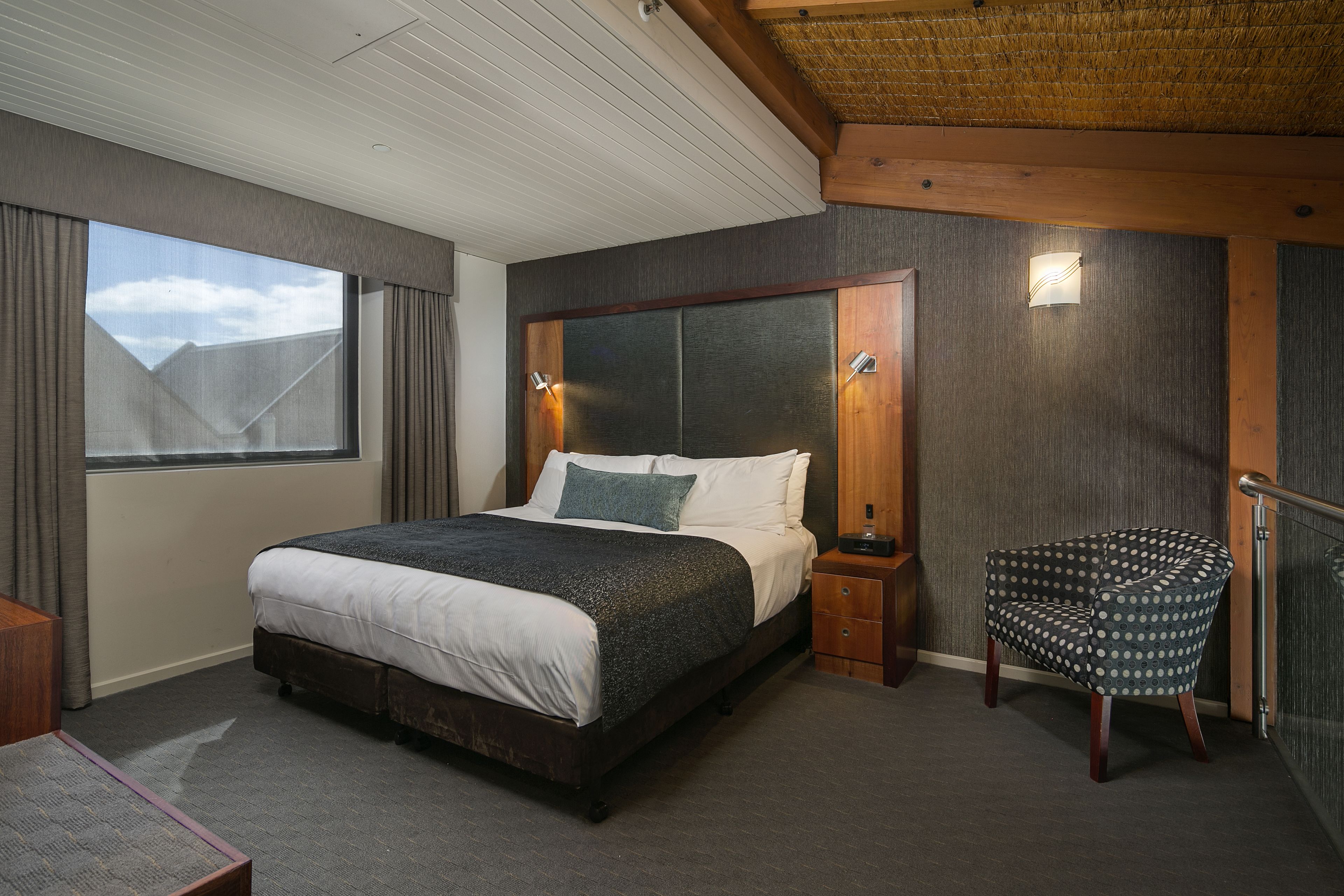 A modern bedroom with a large bed, a wooden headboard, a chair, and a window.