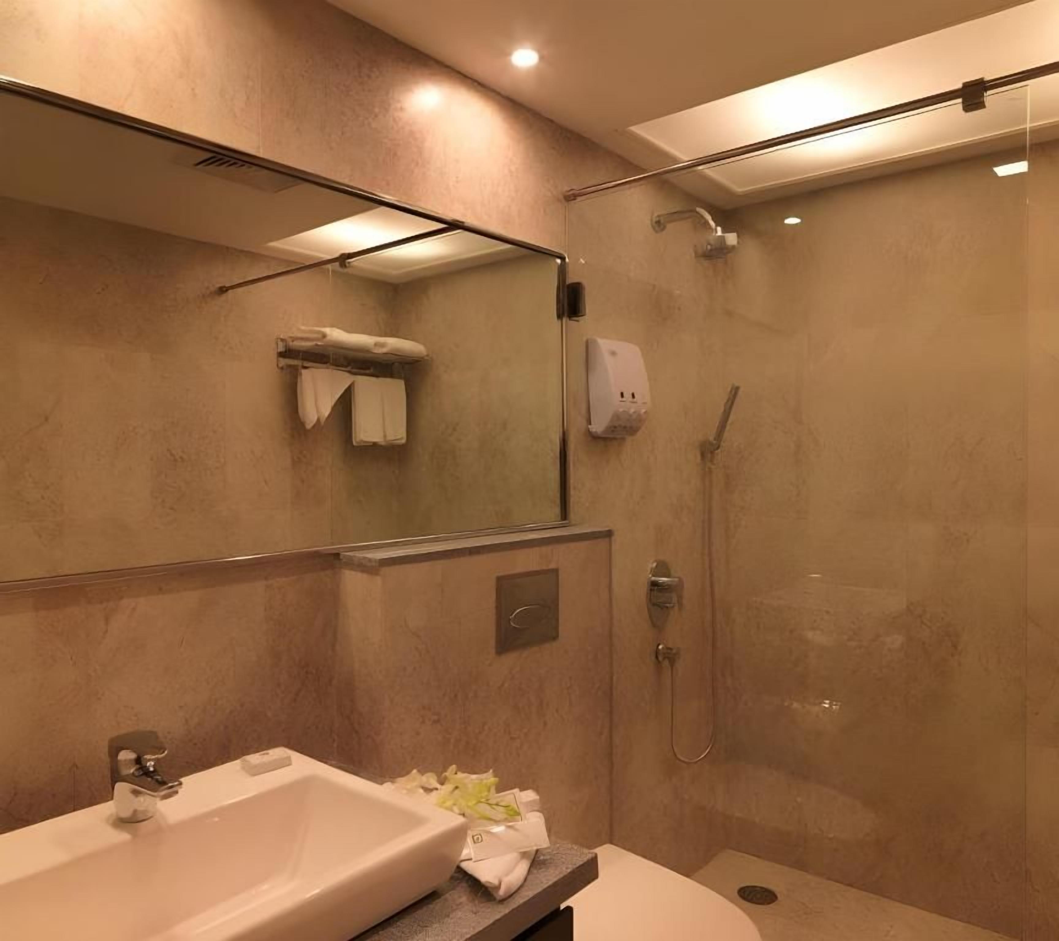 A modern bathroom with a glass-enclosed shower, a sink with a soap dispenser, and a towel rack.