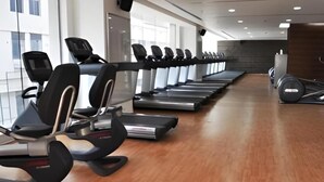 A gym with treadmills aligned along the walls, a wooden floor, and a weight bench area.
