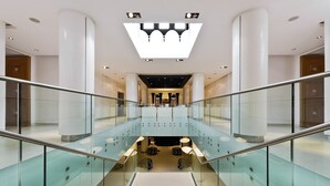 A modern interior with a glass staircase, white columns, and a central light fixture.