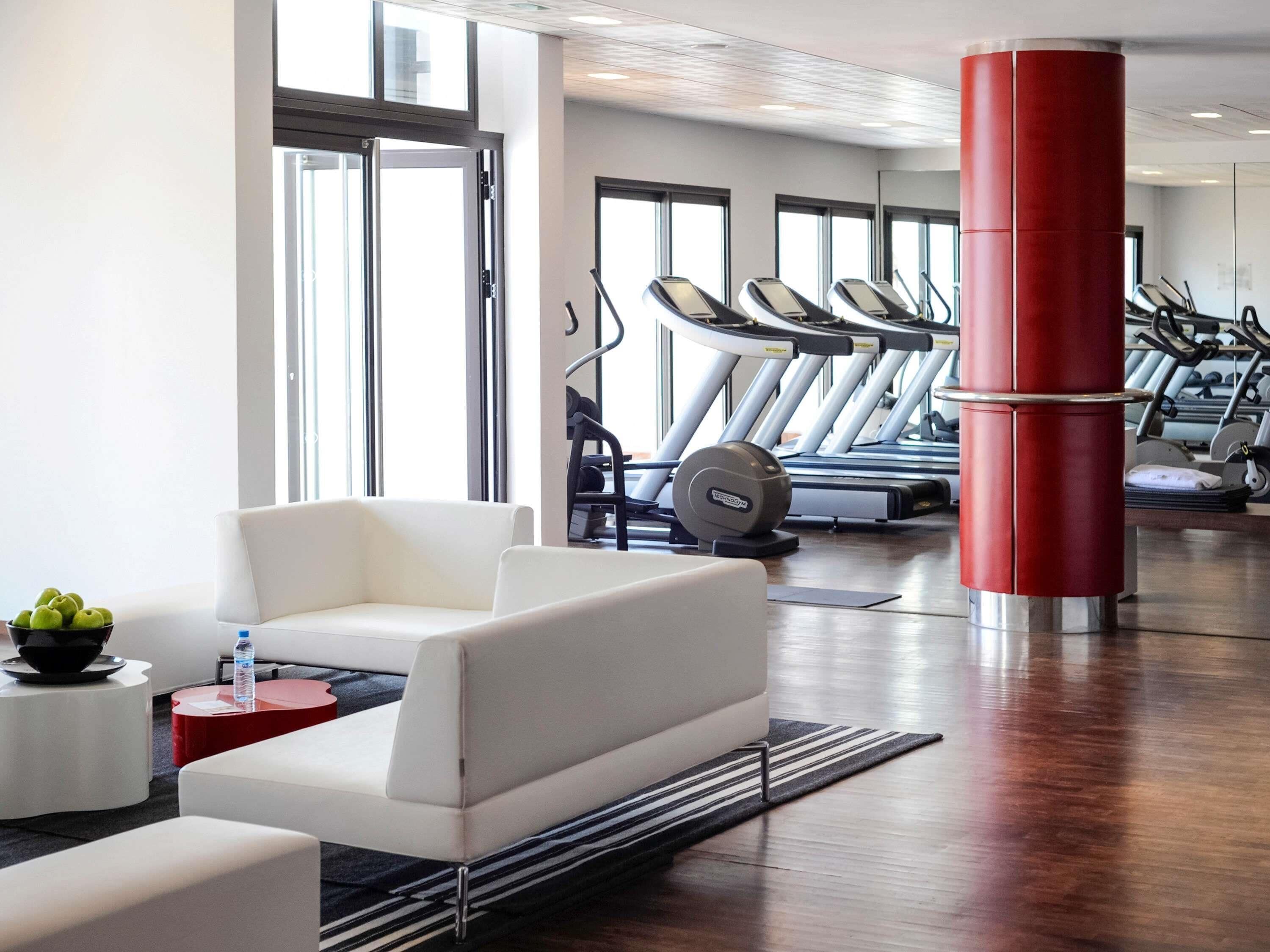 A gym with treadmills, a white sofa, and a red pillar.