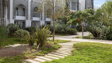 A modern building with multiple balconies, surrounded by well-maintained gardens and a clear pathway.