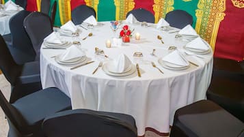 Une table ronde dressée pour un événement officiel, avec des nappes blanches, des chaises noires et des couverts dorés.
