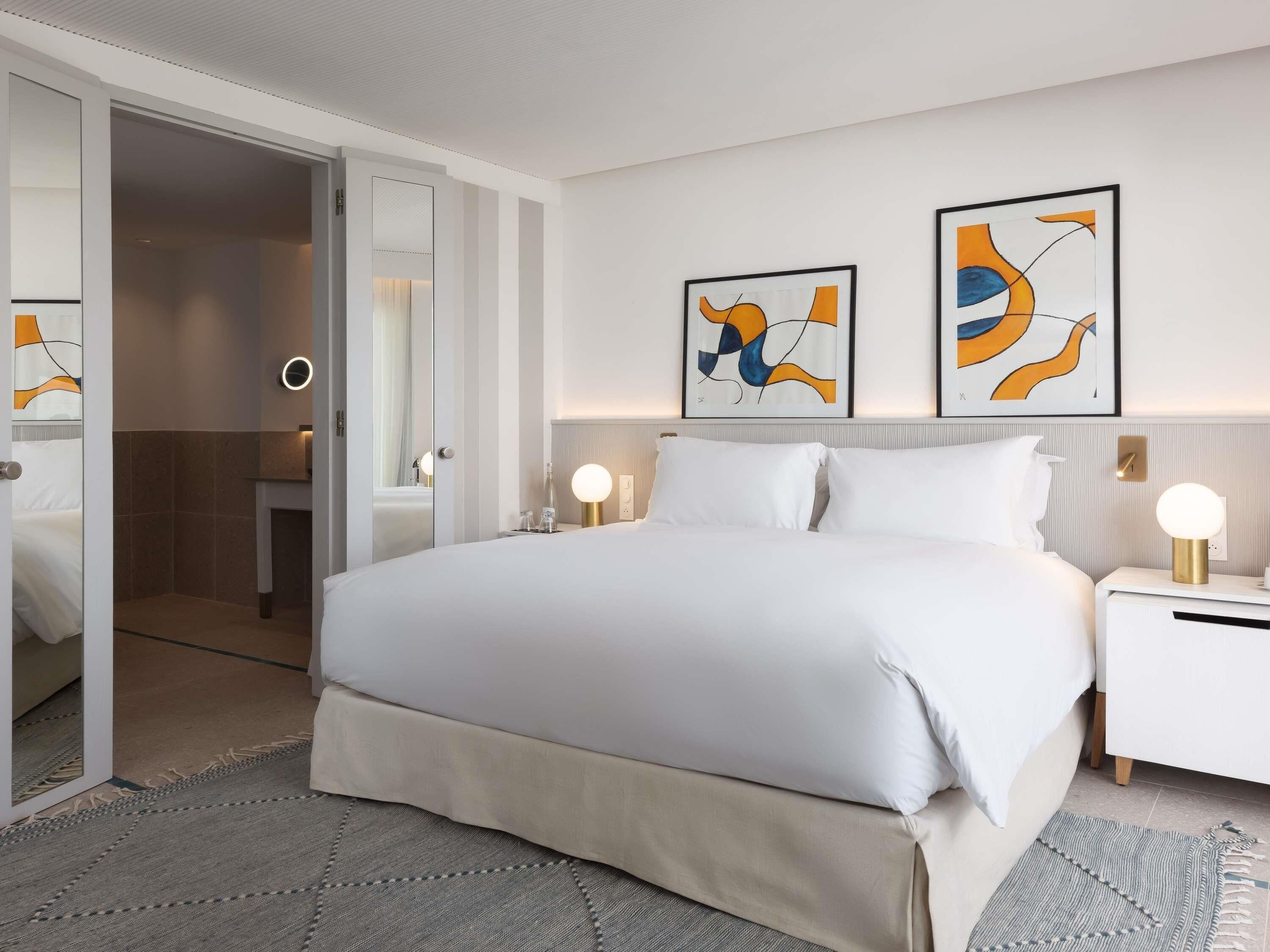 Een moderne hotelkamer met een groot bed, nachtkastjes, een spiegel en abstracte kunst aan de muren.