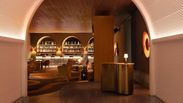 Un bar moderno con techo curvo, una recepción y una zona de estar con mesas y sillas.