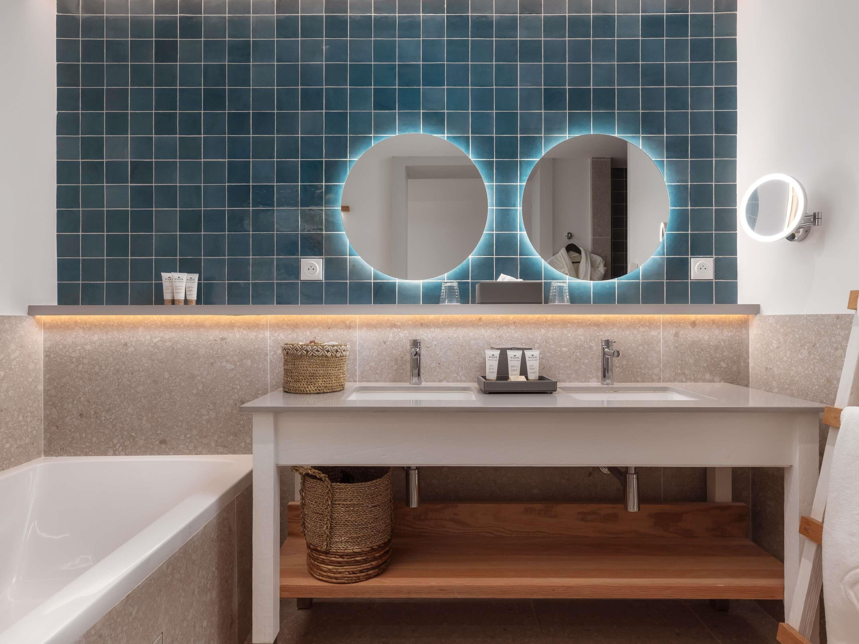 Ein modernes Badezimmer mit einem weißen Waschtisch, zwei runden Spiegeln und einer blauen Fliesenspiegel.