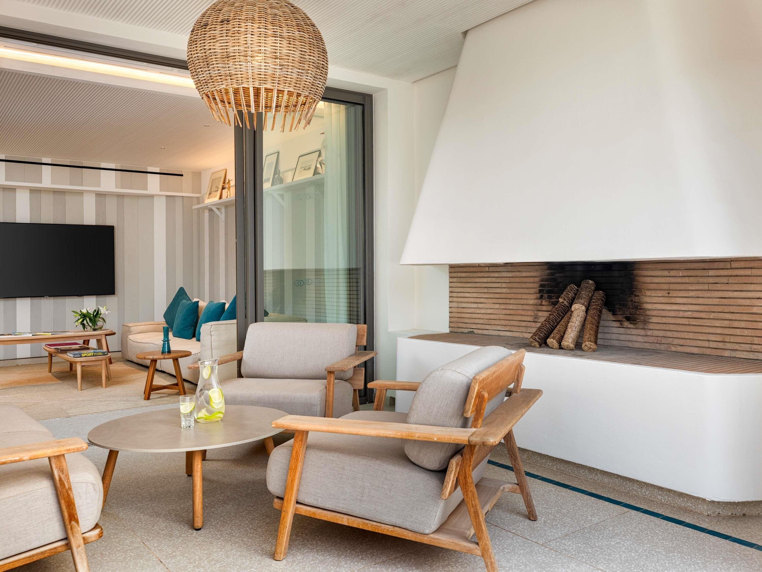 A modern living room with a fireplace, comfortable seating, a flat-screen TV, and a large window.