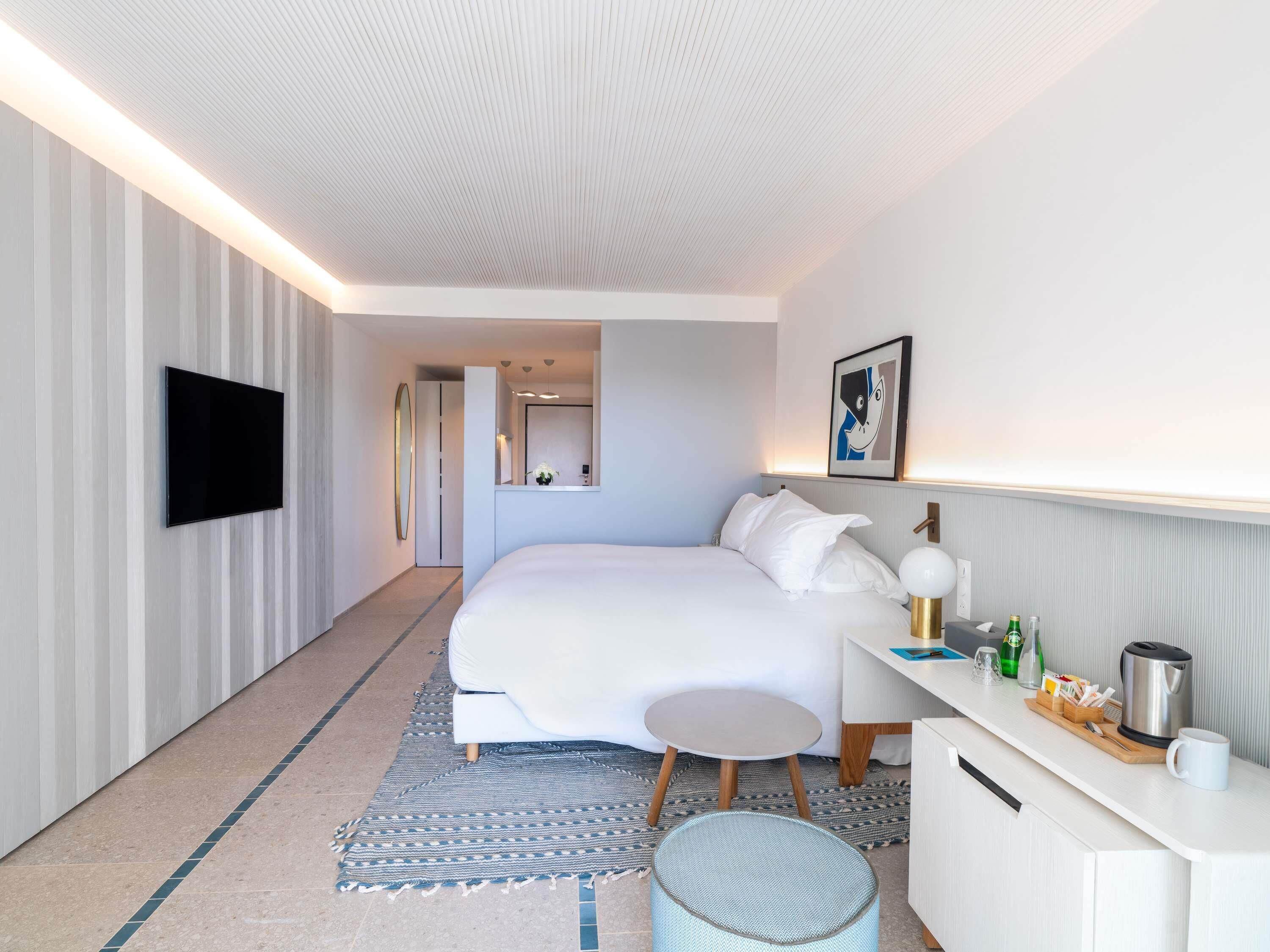 Una habitación de hotel moderna con cama, mesita de noche, televisión y una pequeña zona de estar.