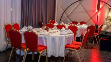 A dining area with round tables, red upholstered chairs, and white tablecloths.