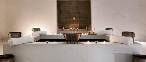 A modern bathroom with a large bathtub, candles, and decorative pots.