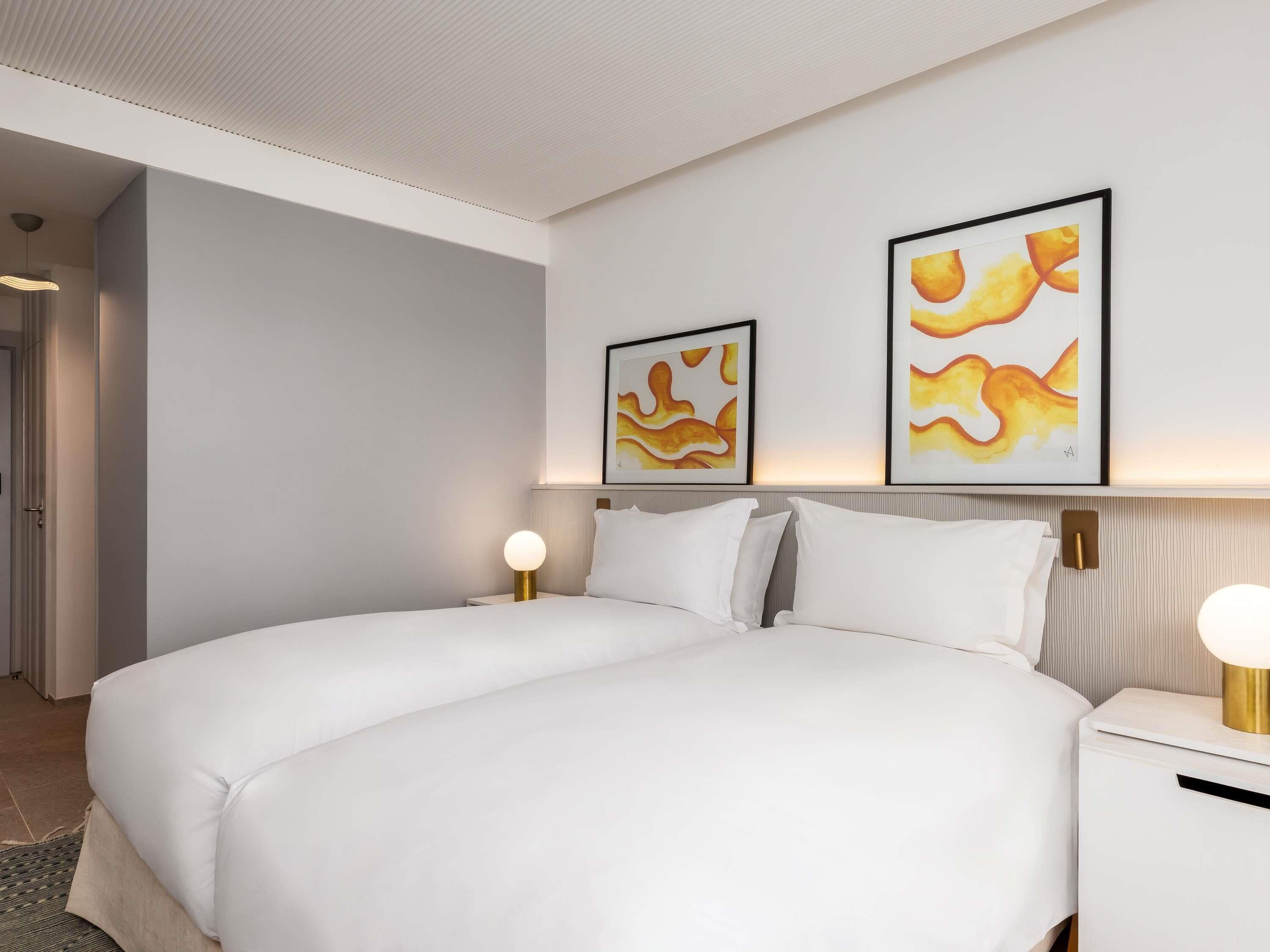 A modern hotel room with a large bed, two bedside tables with lamps, and abstract artwork on the wall.