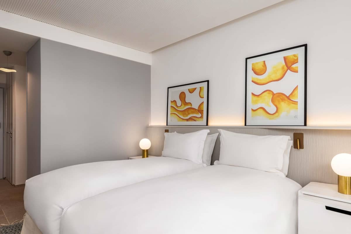 Una habitación de hotel moderna con una cama grande, dos mesitas de noche con lámparas y arte abstracto en la pared.