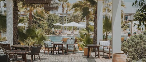 A wooden deck with outdoor seating, a pool, and palm trees.