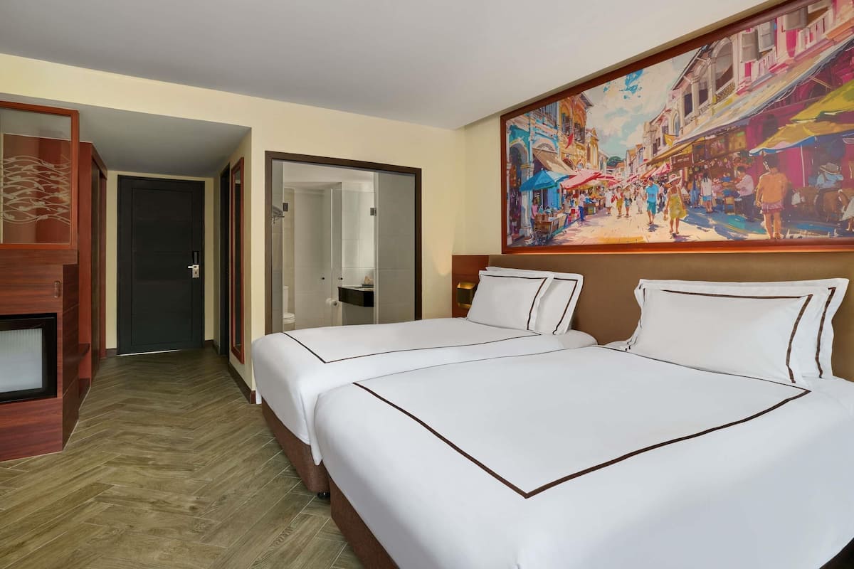 A hotel room with two beds, a painting on the wall, and a wooden floor.