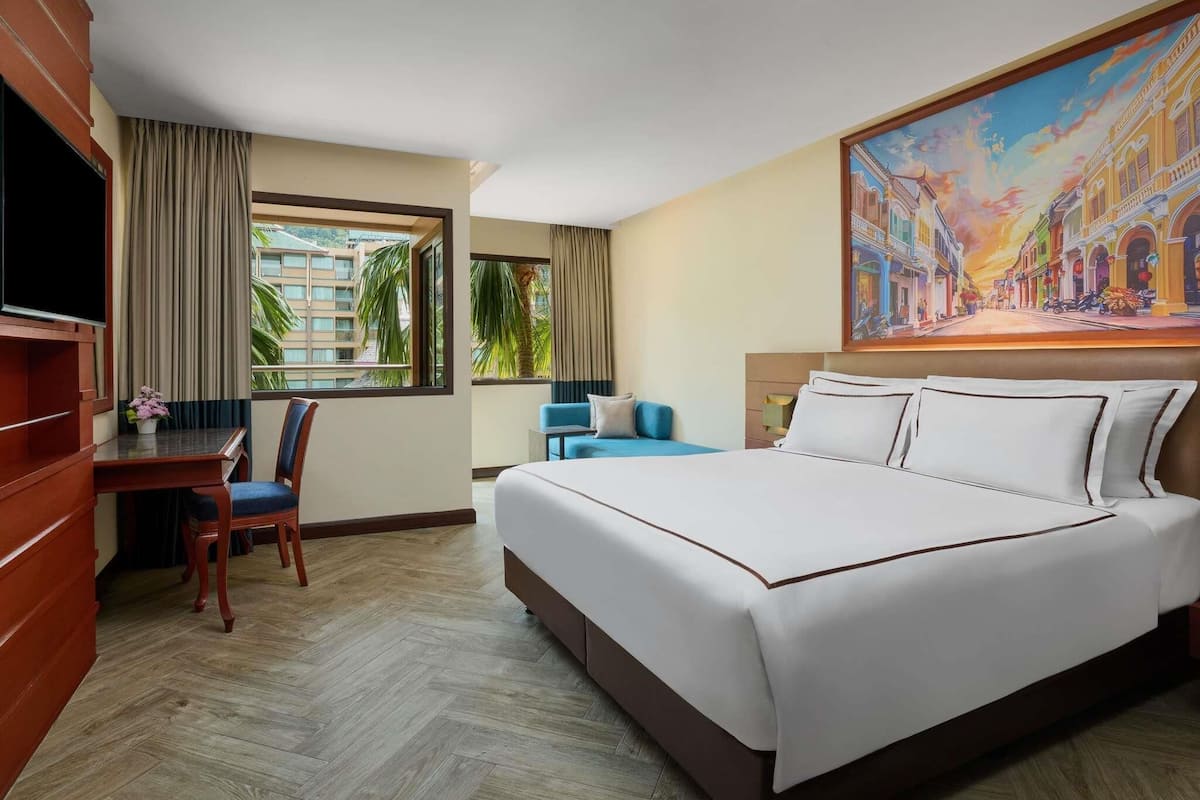 A hotel room with a large bed, a desk with a chair, a TV, and a painting on the wall.