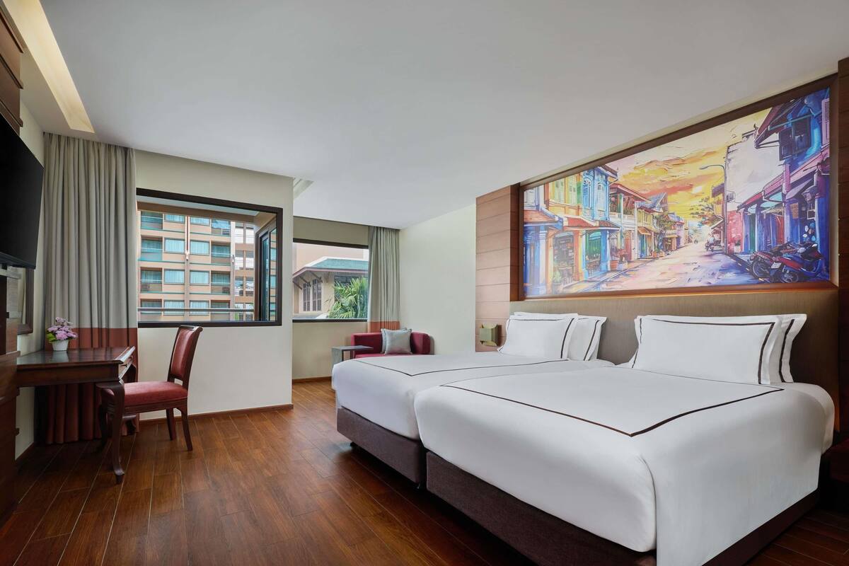 A hotel room with a large bed, a desk, a chair, a window with curtains, and a painting on the wall.