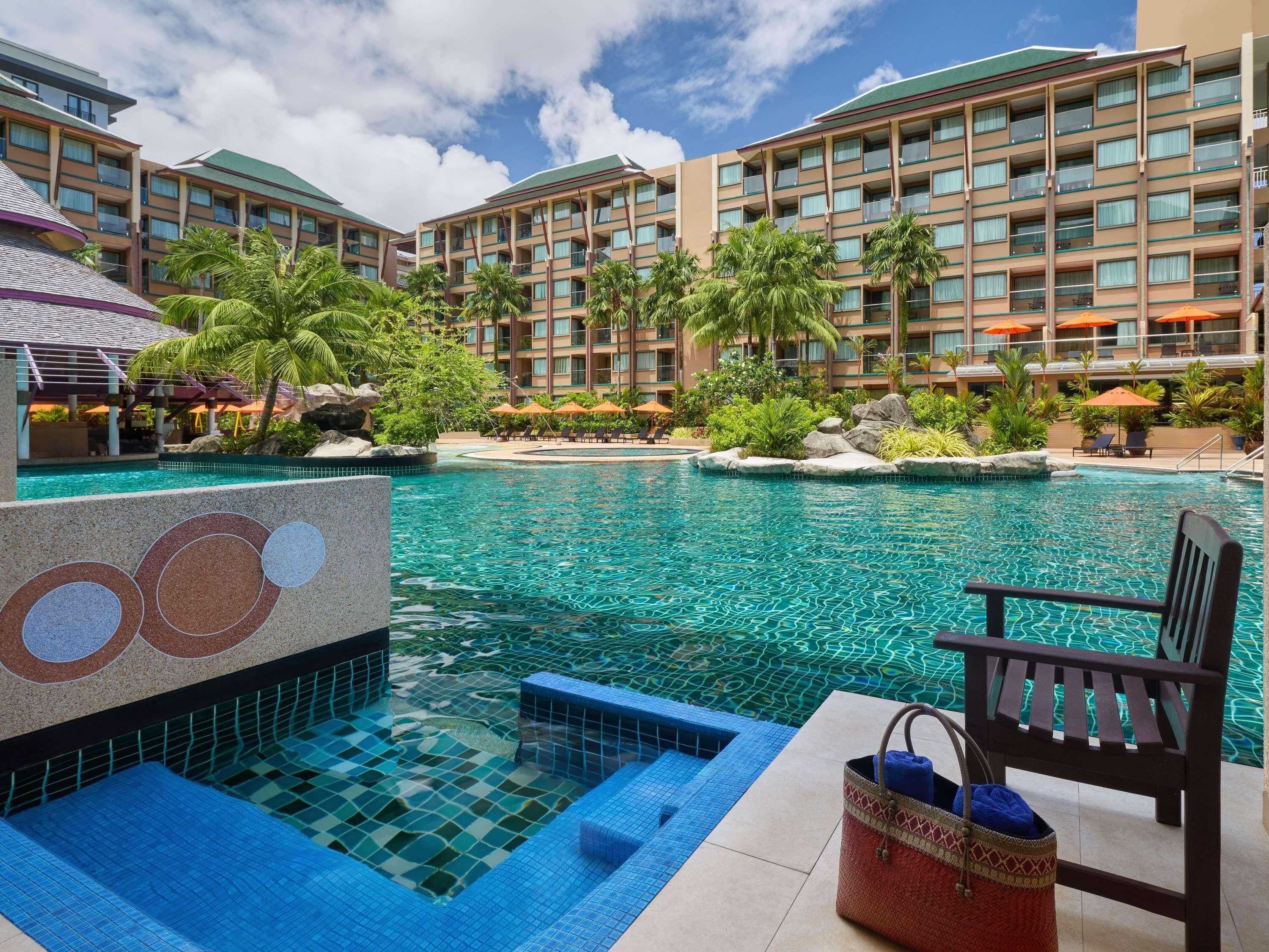 A hotel pool area with multiple swimming pools, lounge chairs, and palm trees.
