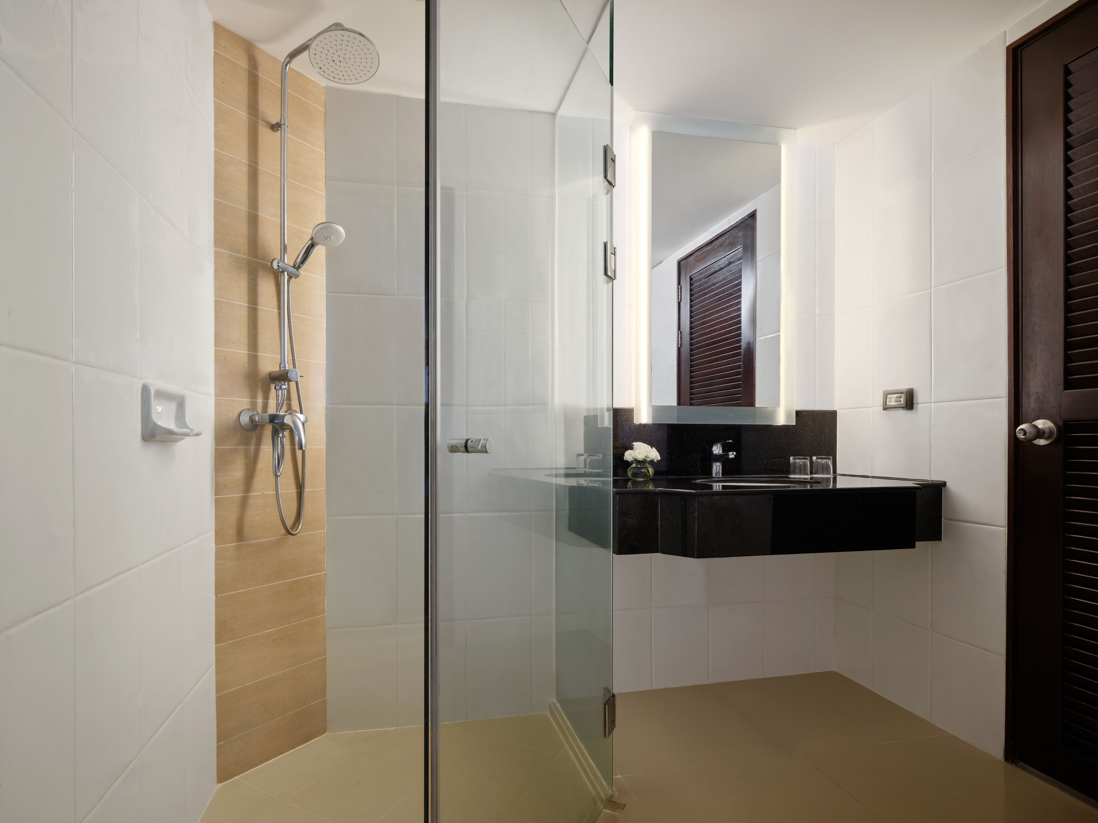 A modern bathroom with a glass-enclosed shower, a black sink vanity, and a wooden door.