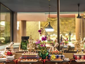 A restaurant interior with Buddha statues, a buffet table, and a large window.