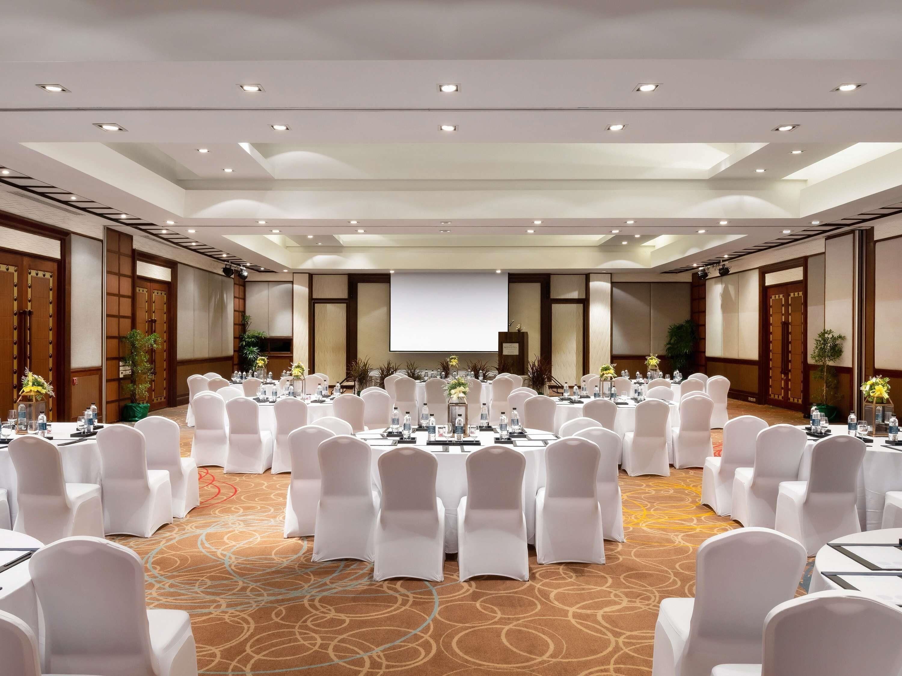A conference room with round tables, white chairs, and a large screen at the front.
