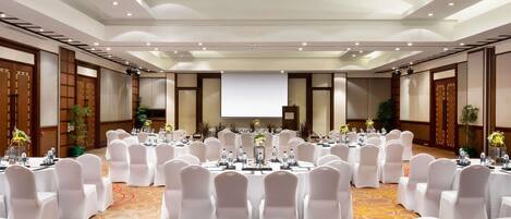 A conference room with round tables, white chairs, and a large screen at the front.