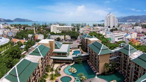 Un resort con varias edificaciones, un área de piscina central y vista al mar.