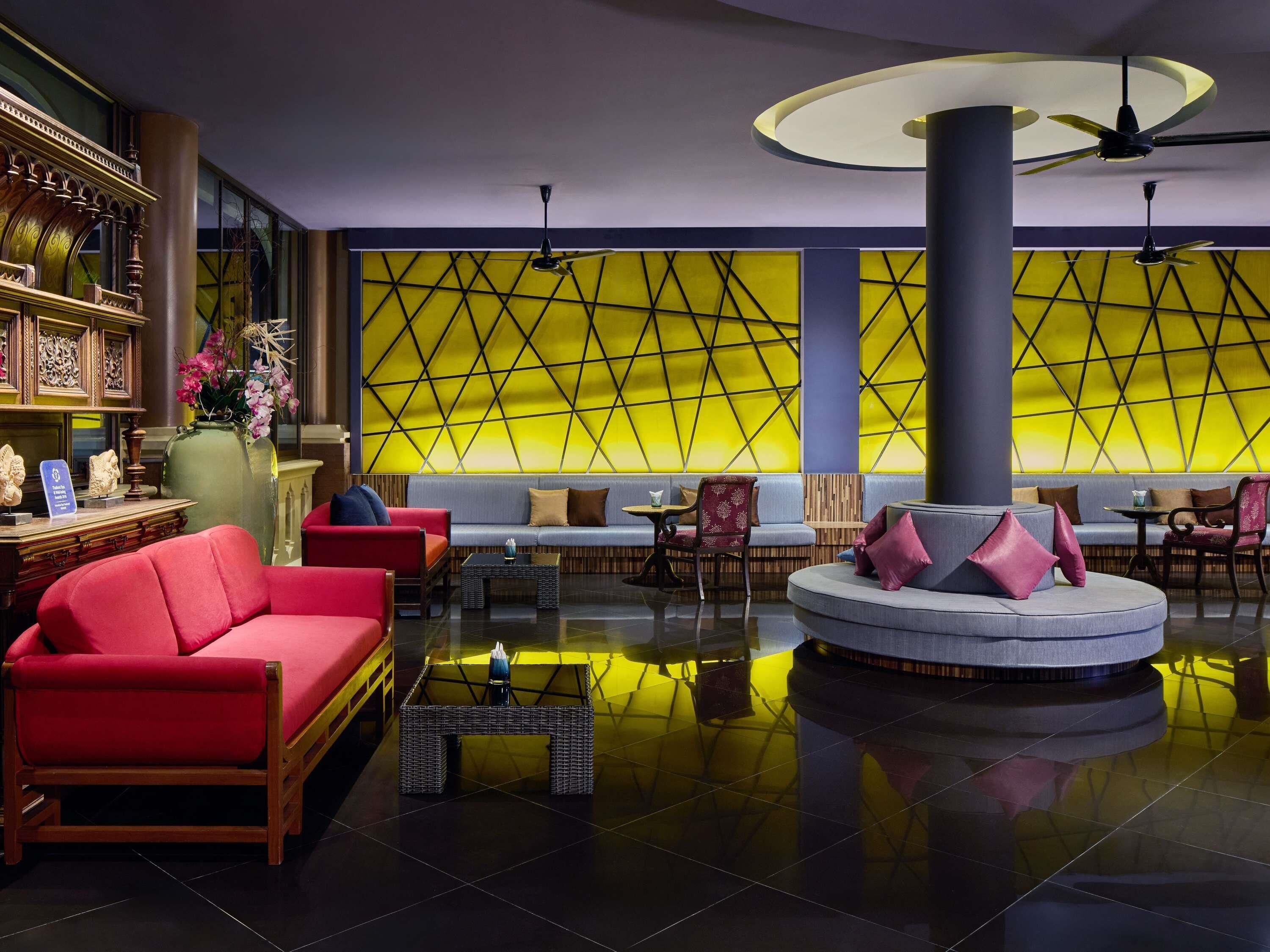 A modern lobby with a central seating area, a decorative wall with geometric patterns, and a ceiling fan.