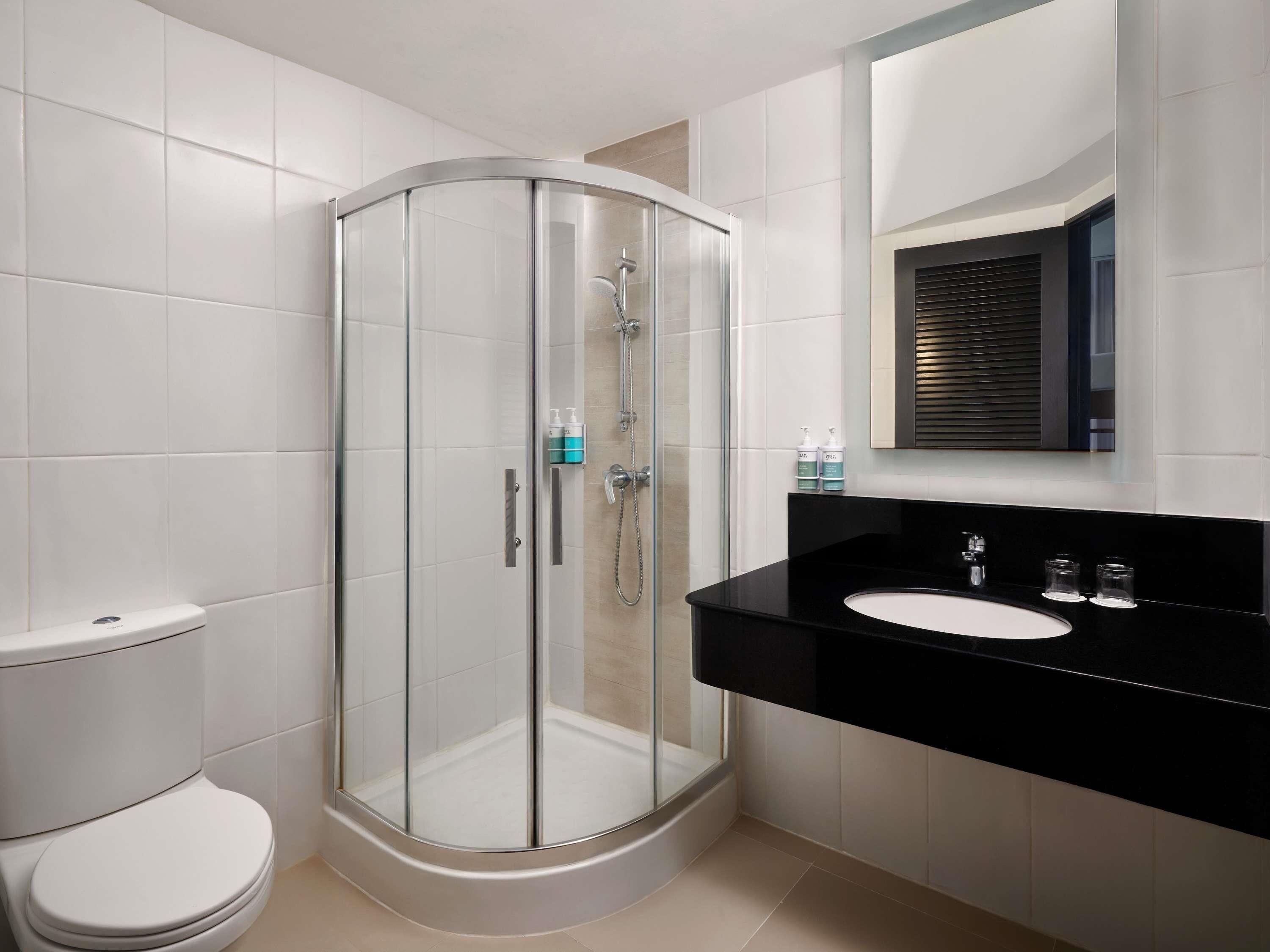 A modern bathroom with a glass-enclosed shower, a black sink, and a toilet.