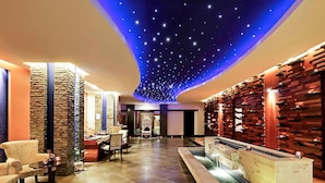 Un vestíbulo de hotel con techo estrellado, una recepción, una zona de estar y una pared decorativa con estanterías.