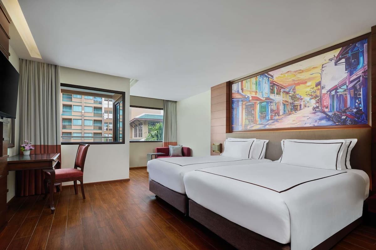 A hotel room with a large bed, a desk, a chair, and a painting of a street scene.