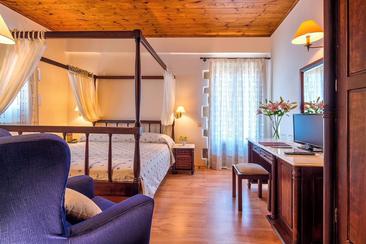 A bedroom with a four-poster bed, a desk with a computer, and a chair.