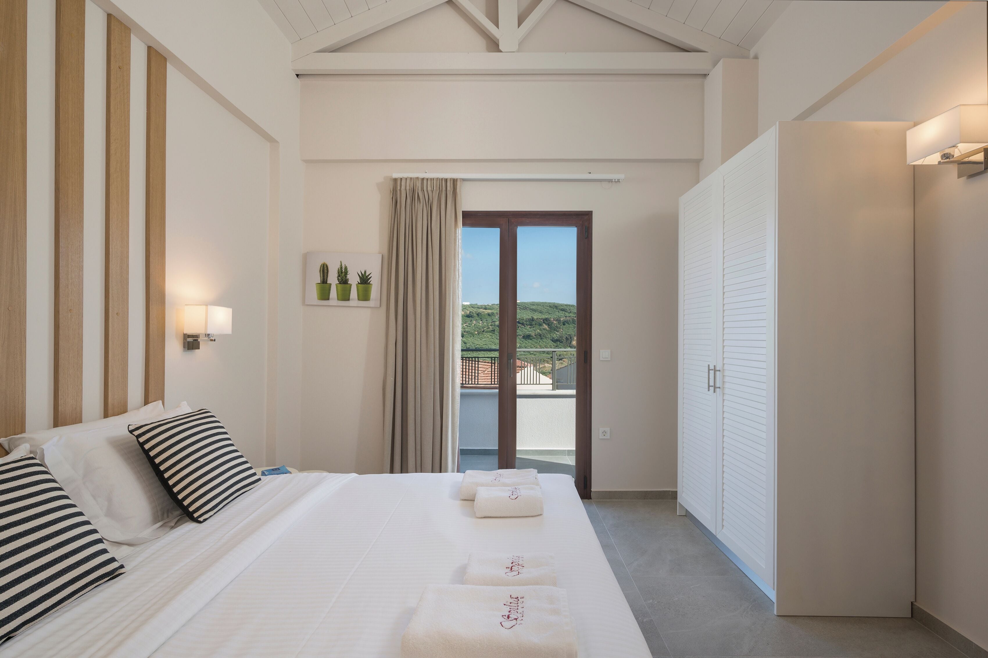 A hotel room with a large bed, a sliding glass door to a balcony, and a view of greenery.