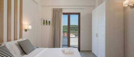 A hotel room with a large bed, a sliding glass door to a balcony, and a view of greenery.