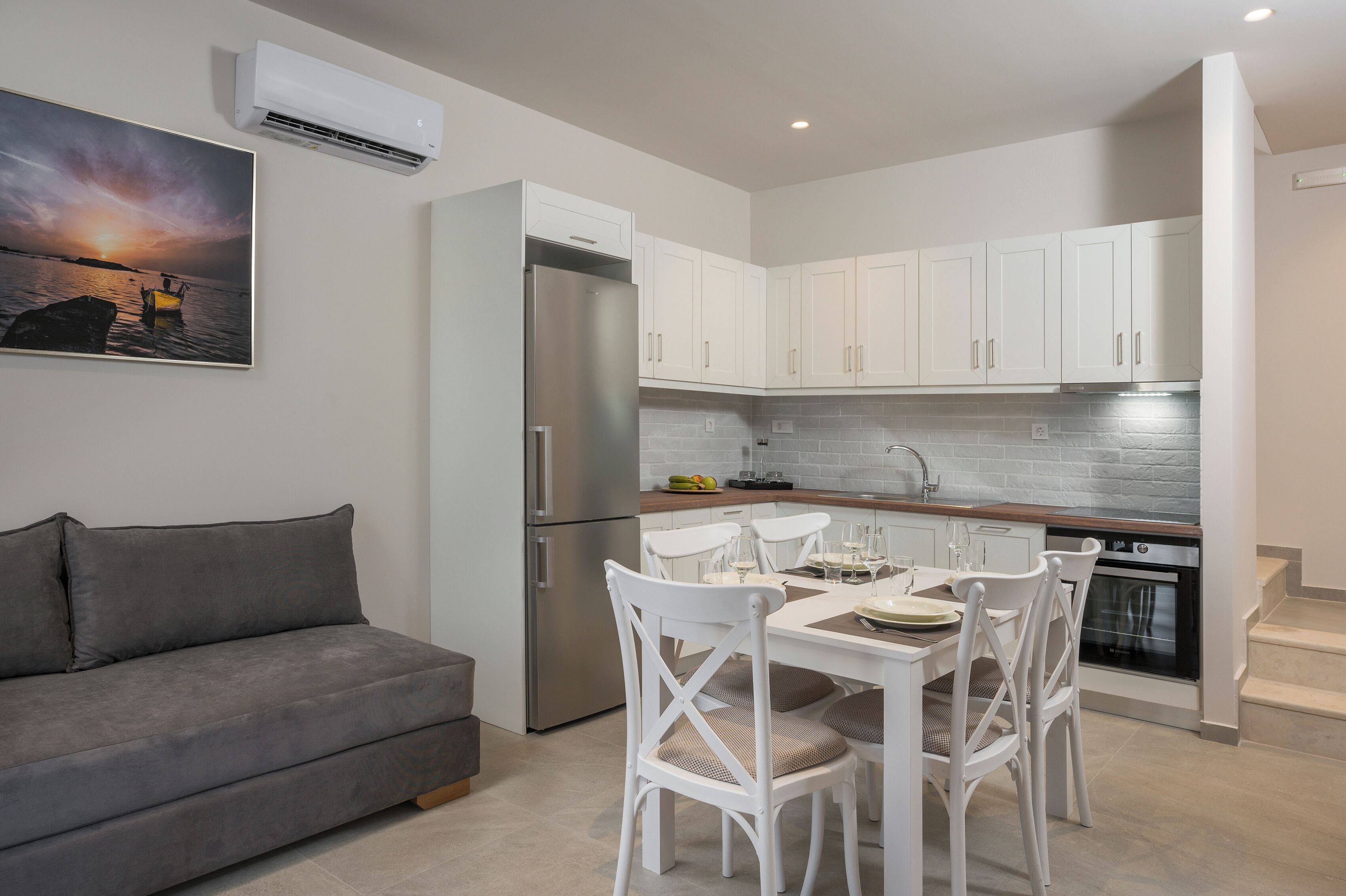 Una cocina moderna con armarios blancos, un refrigerador de acero inoxidable y un comedor con sillas y mesa blancos.