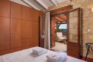 A bedroom with wooden cabinets, a bed with towels, and a view of an outdoor seating area through an open door.