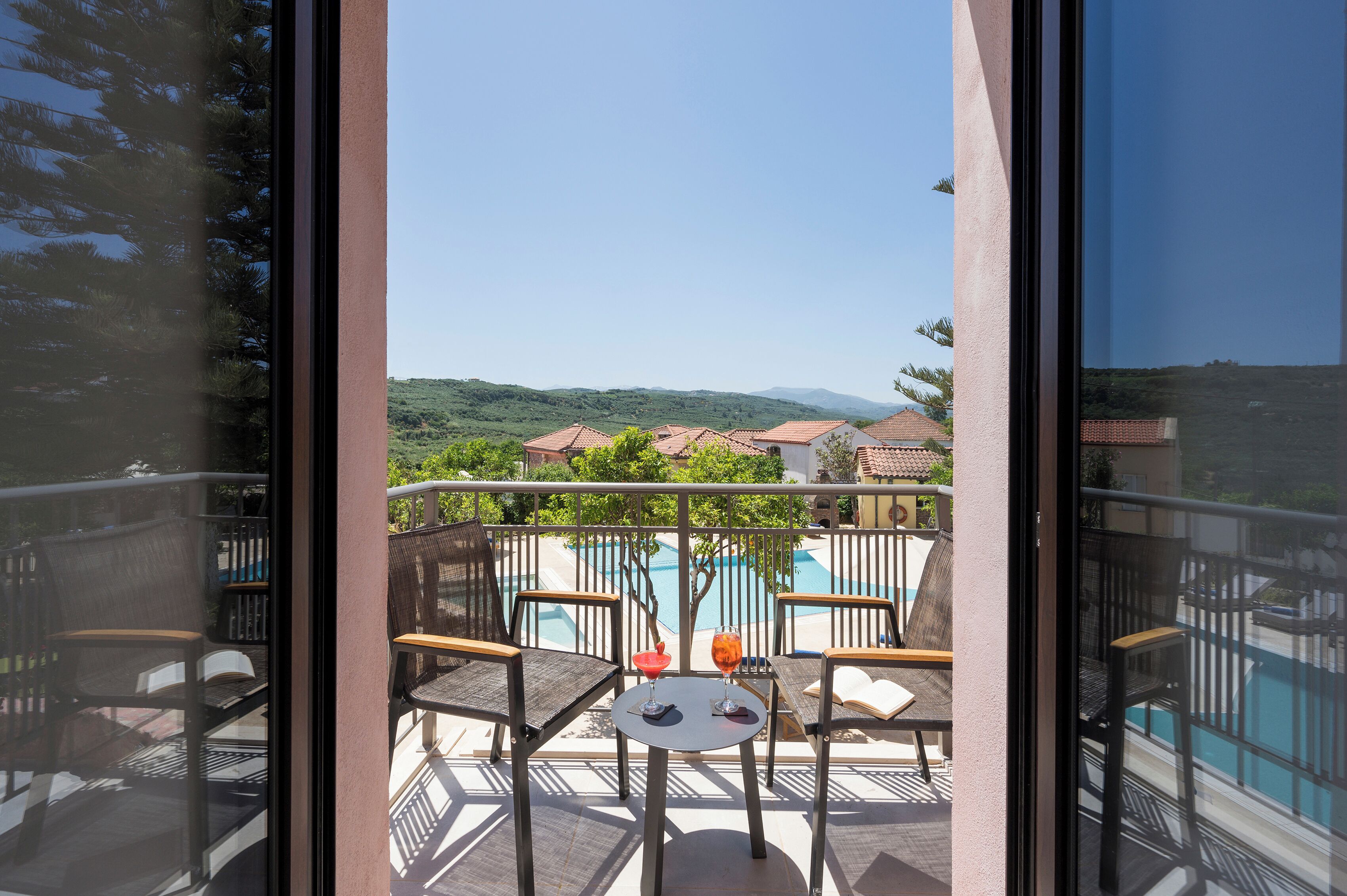 A balcony with a view of a swimming pool and distant hills.