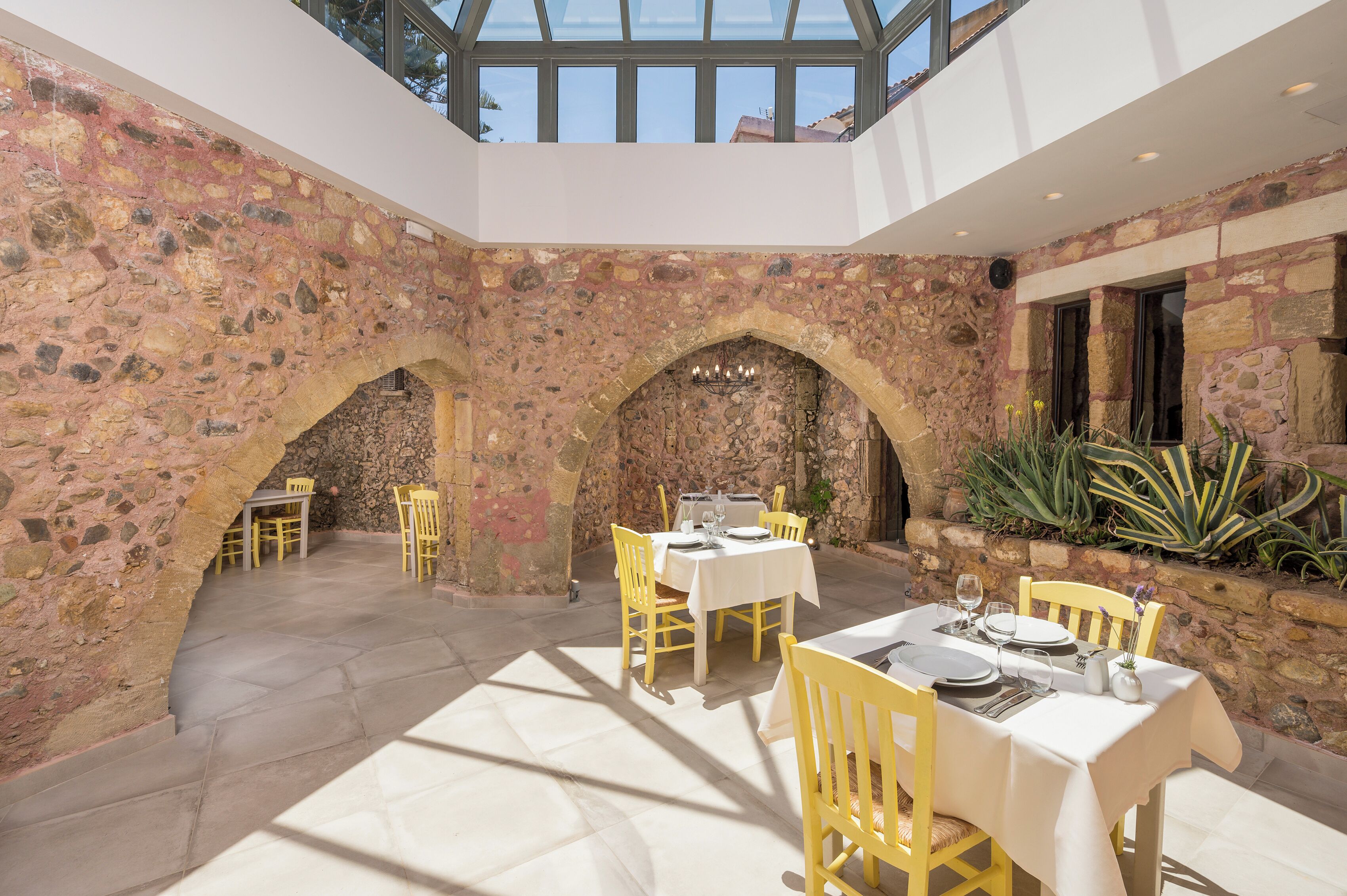 A dining area with stone walls, yellow chairs, and tables set for two.