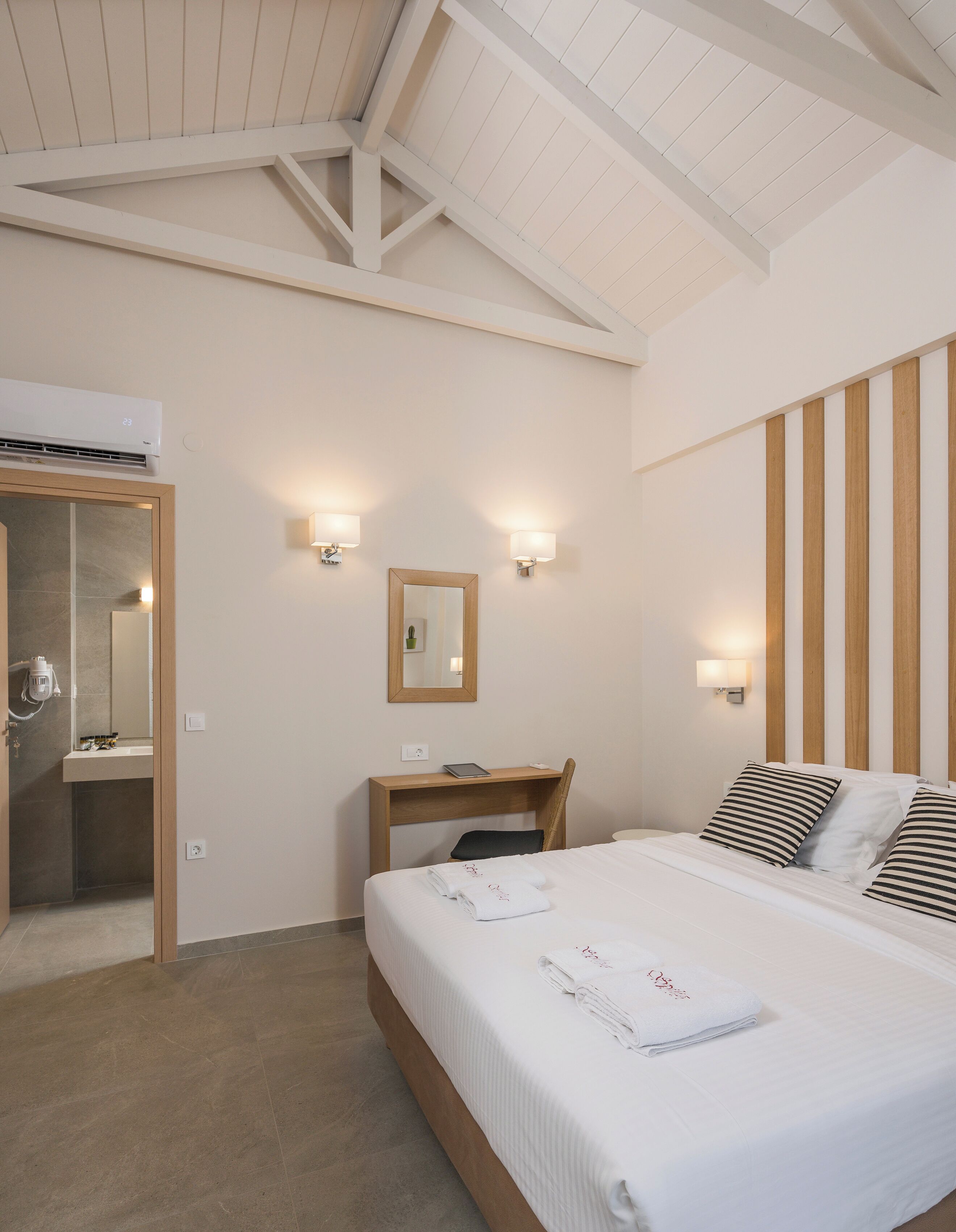 A hotel room with a bed, a desk, a mirror, and a shower area.