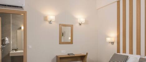 A hotel room with a bed, a desk, a mirror, and a shower area.