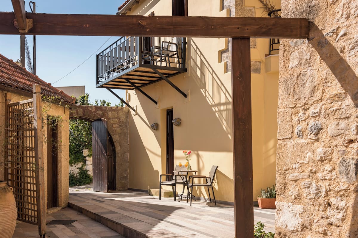A courtyard with a wooden pergola, a balcony, and a table with chairs.