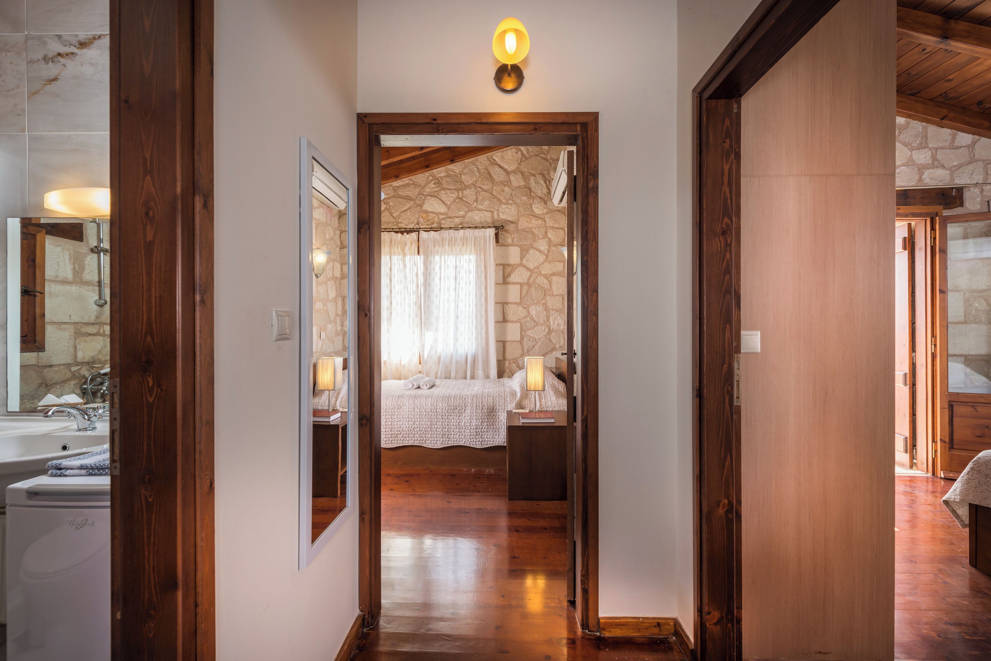 A hallway leading to a bedroom with a stone wall, wooden flooring, and a bed with a white bedspread.