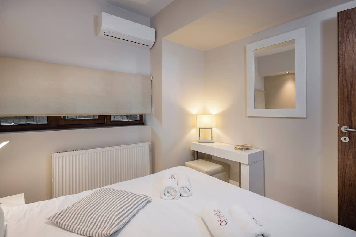 A hotel room with a bed, a bedside table with a lamp, a mirror, a radiator, and a wooden door.
