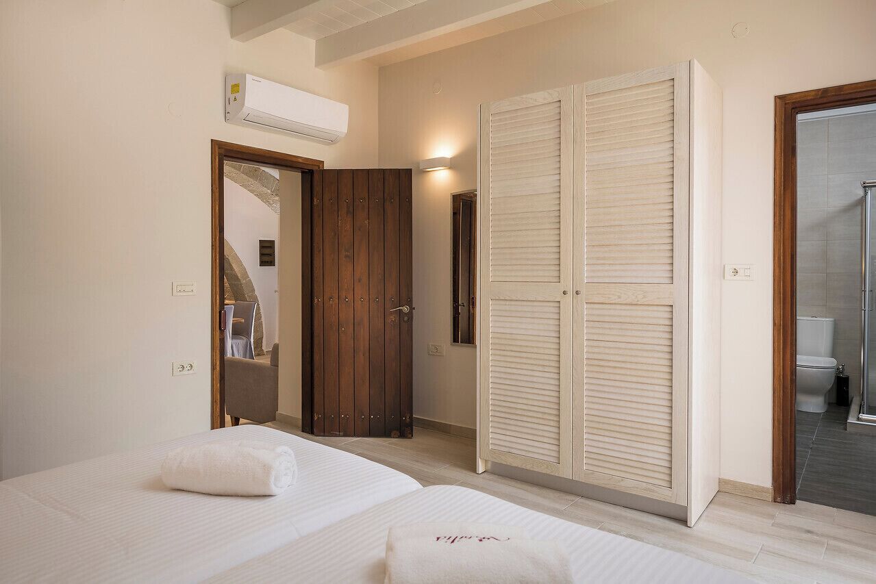 A bedroom with two beds, a wooden wardrobe, a mirror, and an air conditioning unit.
