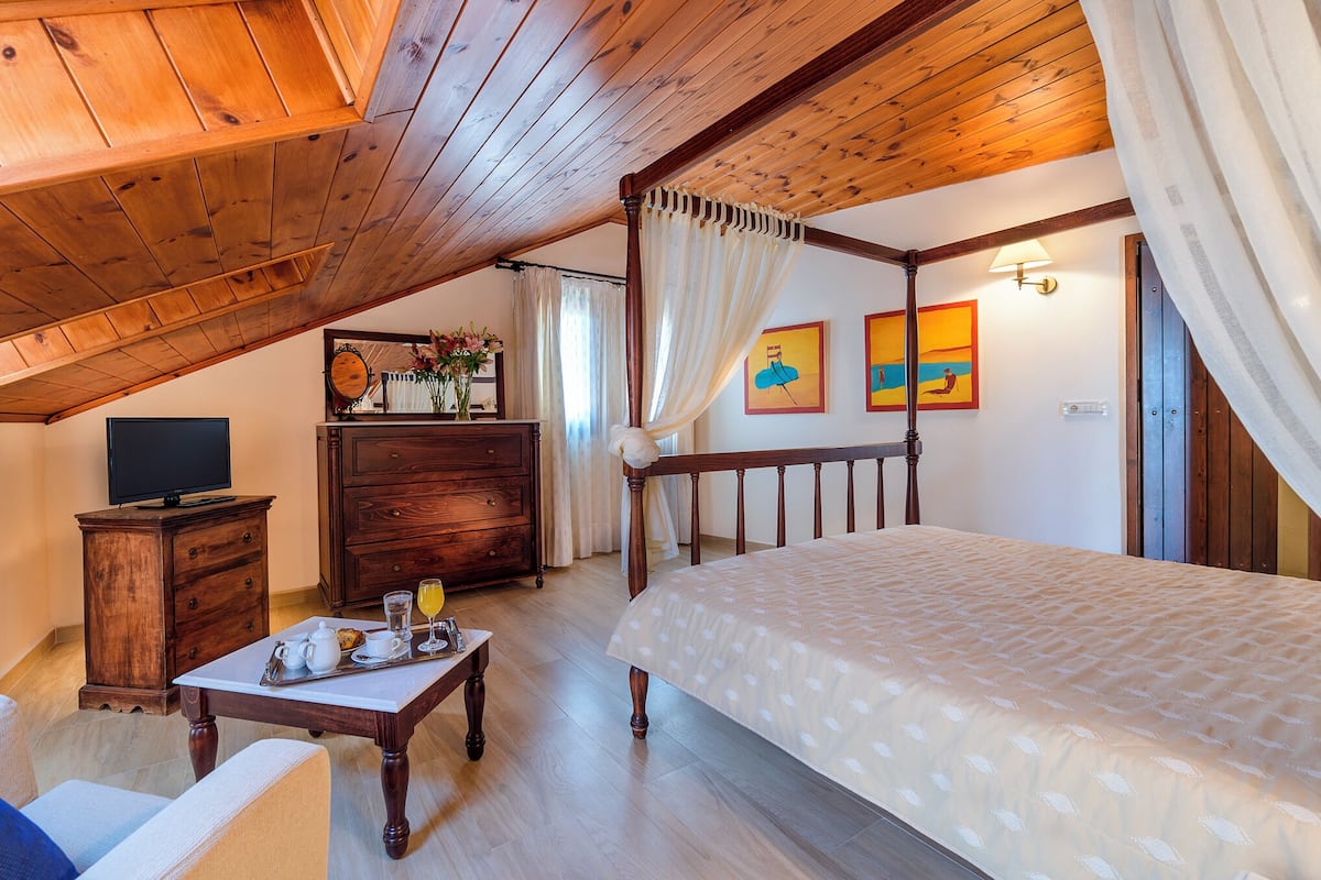 A cozy bedroom with a wooden ceiling, a four-poster bed, a wooden dresser, a television, and artwork on the walls.