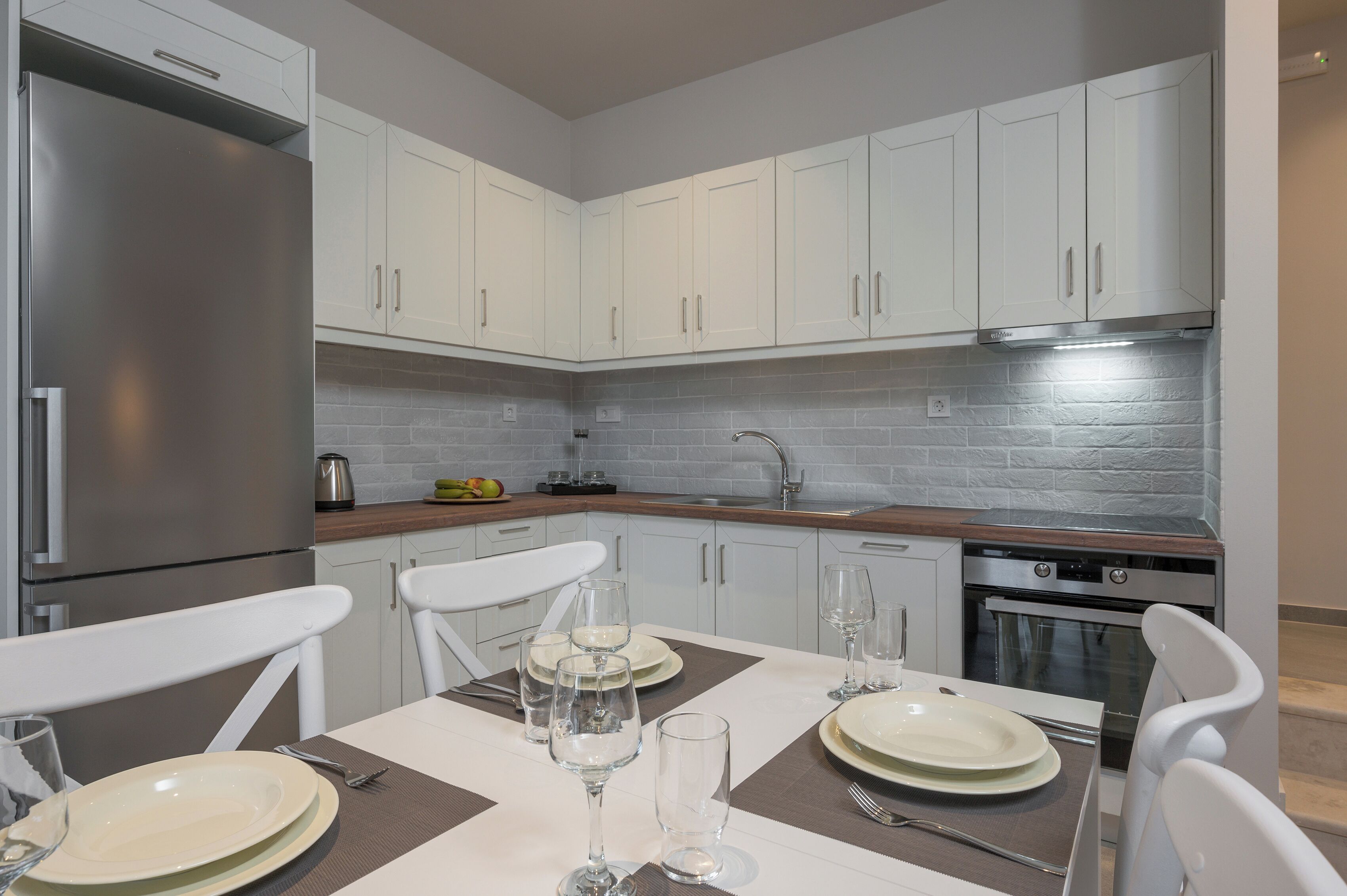 A modern kitchen with white cabinets, stainless steel appliances, and a dining table set for four.