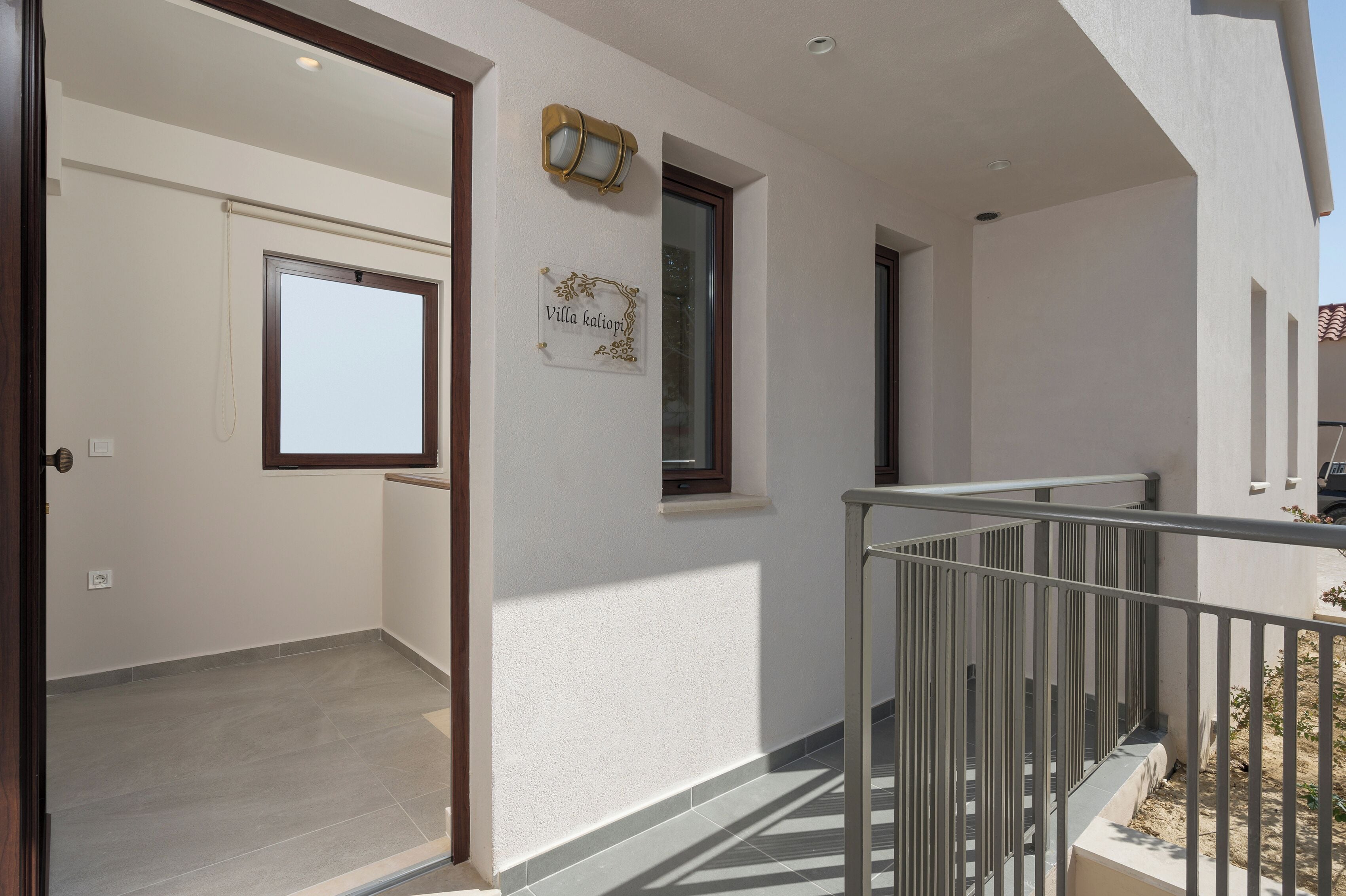 Une entrée propre et moderne, dotée d’une porte vitrée, d’une petite fenêtre ornée d’une enseigne décorative et d’une rambarde métallique menant à un balcon.