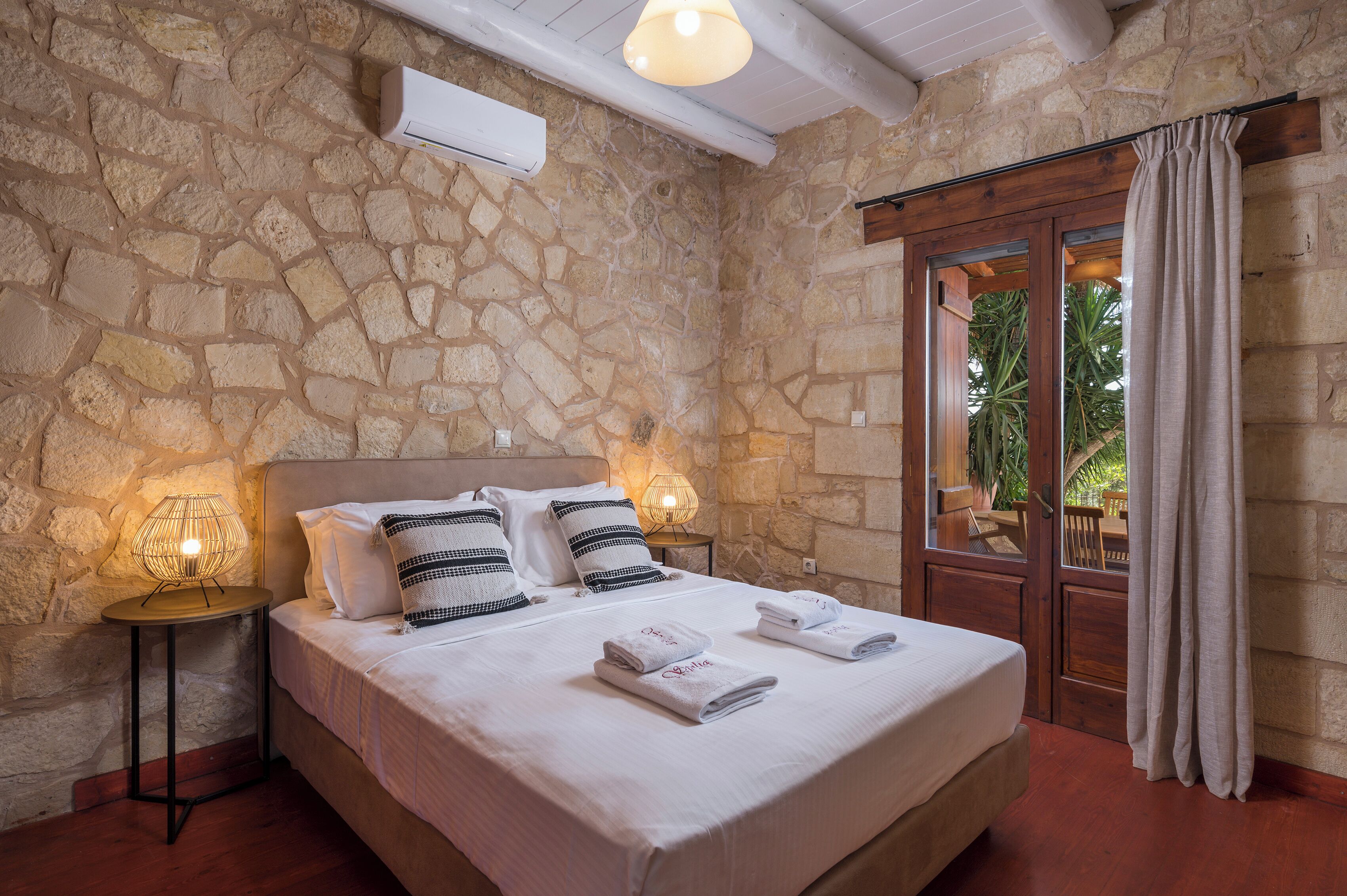 Un dormitorio con paredes de piedra, una cama, dos lámparas de noche y vistas por una puerta.
