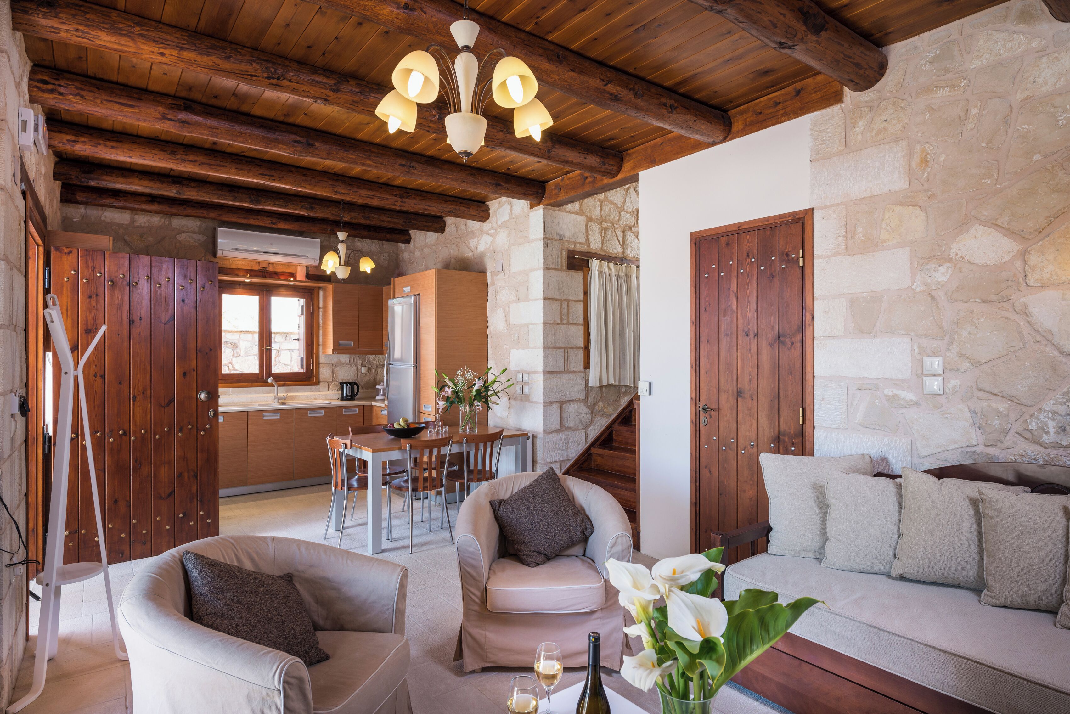 Un espacio de sala de estar acogedor con pared de piedra, vigas de madera en el techo, un sofá, una silla y una mesa de comedor con sillas.