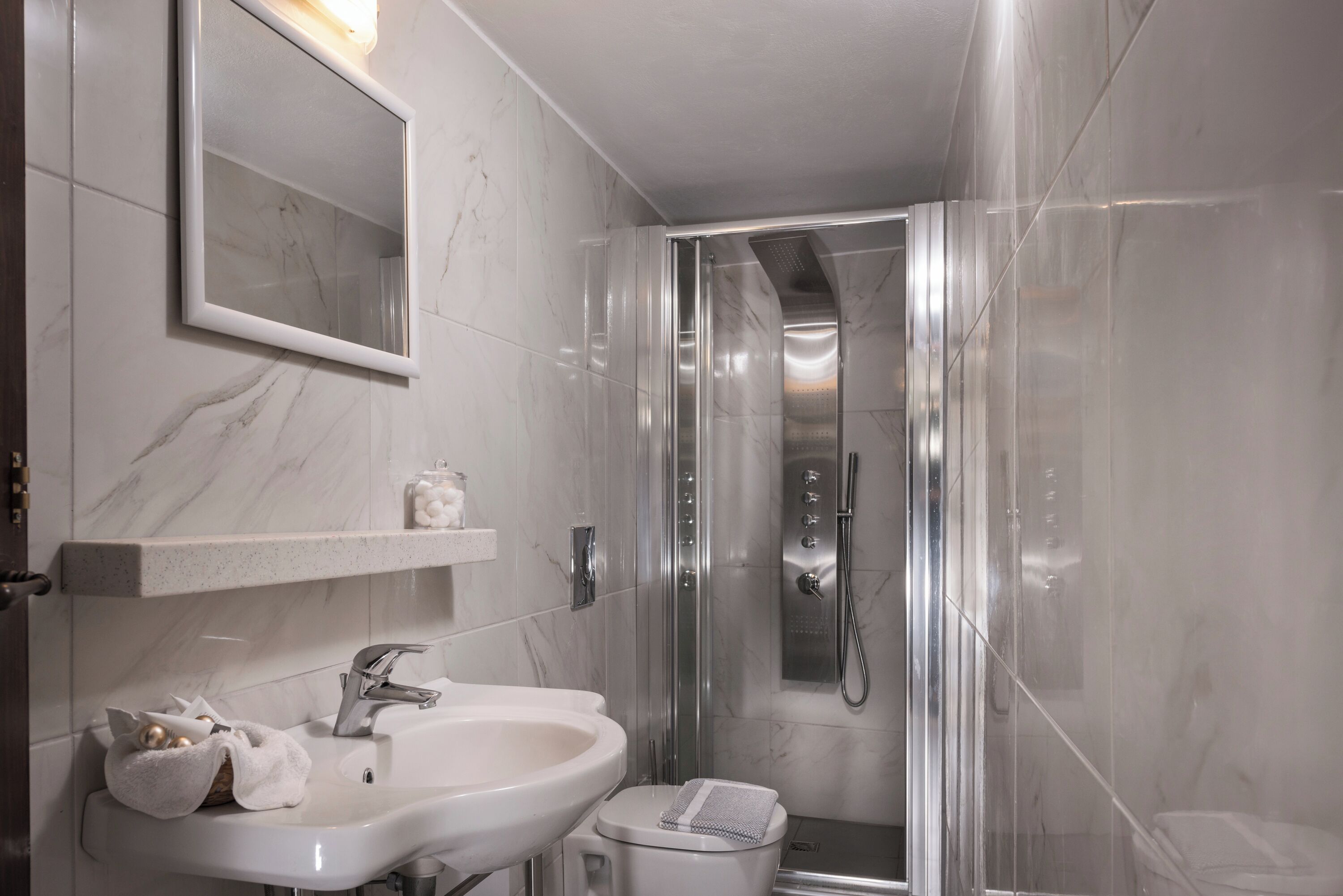 A modern bathroom with a marble sink, a mirror, a shower enclosure, and a toilet.