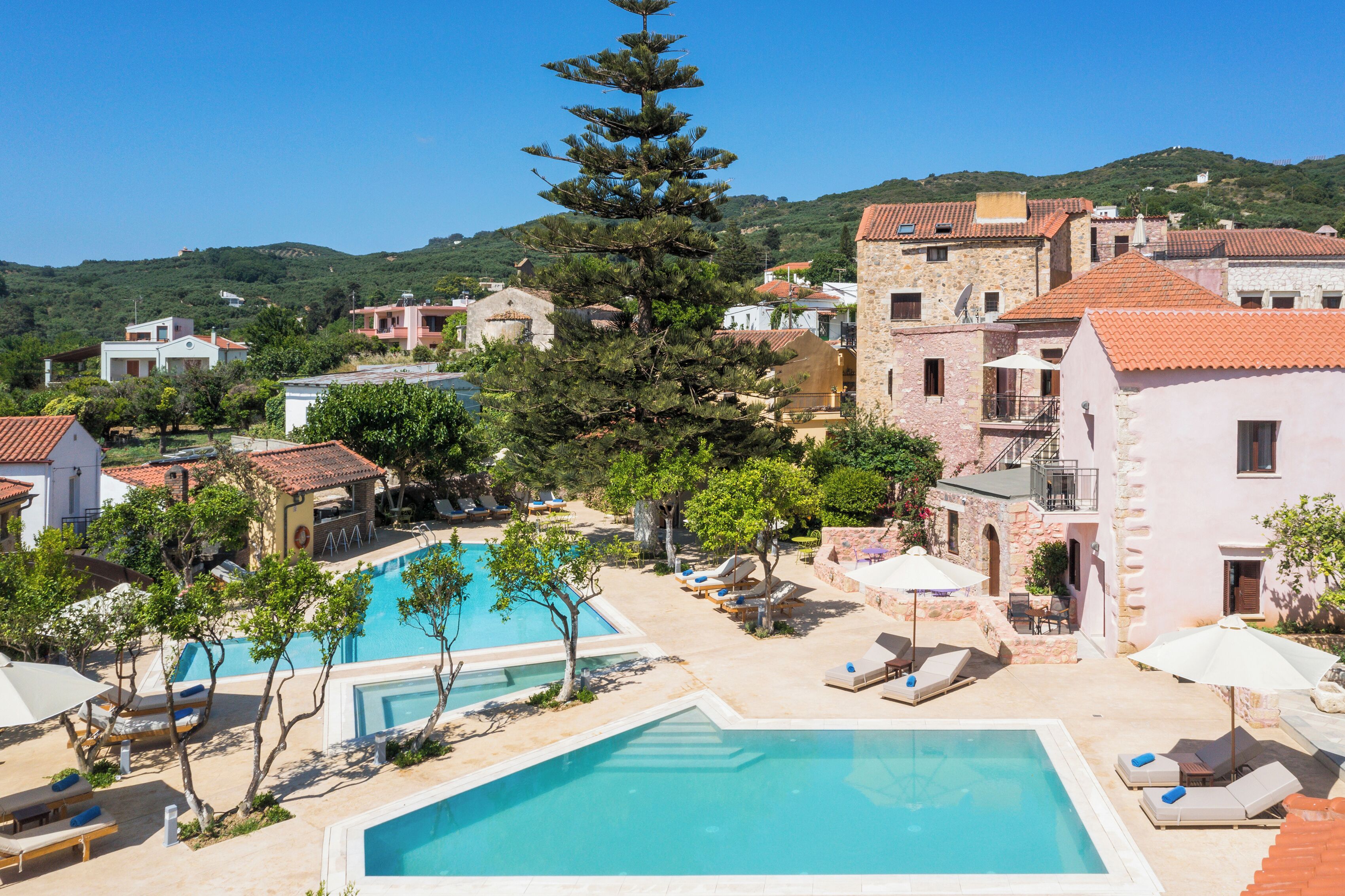 Un resort con piscina central, sillas de descanso y montañas al fondo.